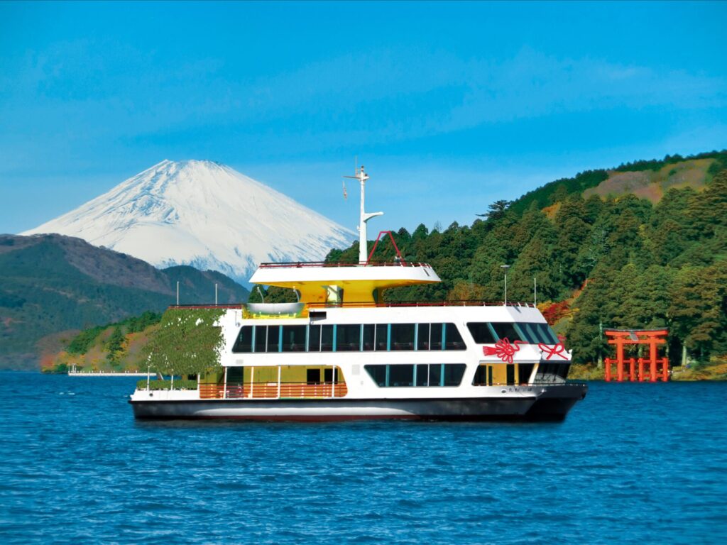 箱根の大自然のなか、芦ノ湖をゆったりと進む、箱根遊船 SORAKAZE。船の奥には雪の積もった富士山が見える。
