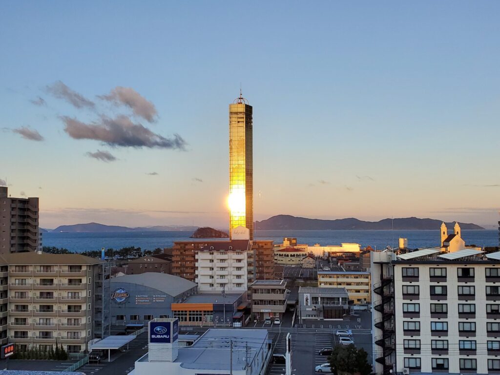 朝焼けに照らされ金色に輝くゴールドタワー。手前には宇多津町のマンション群、奥には瀬戸内海と島々が映っています。