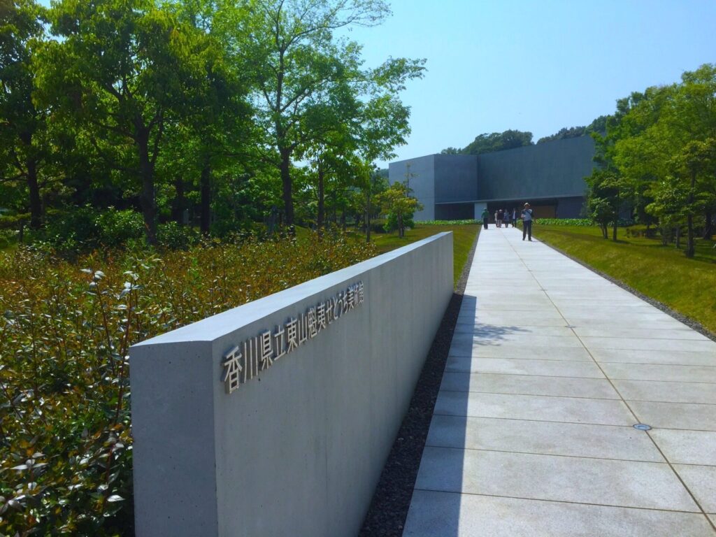 香川県立東山魁夷せとうち美術館入口からまでの通路。手前に美術館の名前が記された石看板、奥には美術館の建物が映っています。