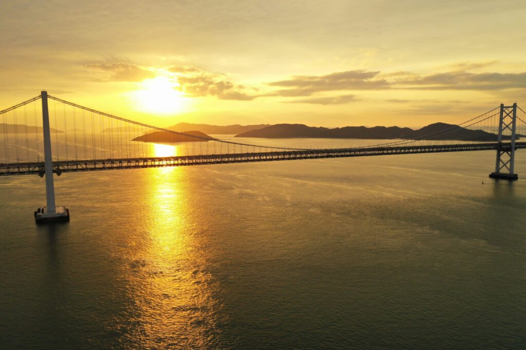 夕焼けに染まる瀬戸内海と瀬戸大橋。夕日が海面でリフレクションしていて、一帯が黄金色に輝いています。