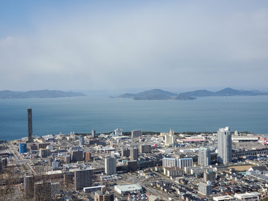 宇多津町の街並みと左にはゴールドタワー、奥には瀬戸内海とそこに浮かぶ島々が映っています。