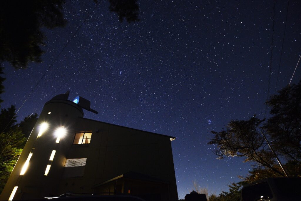 手前にまんのう天文台の建物、奥にはと満天の星空が映っています。