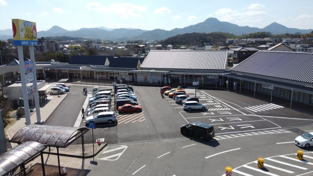 高台から見た道の駅「滝宮」の駐車場と建物の全景。駐車場には数多くの車が止まっており、写真左手には「うどんといちごの郷」と書かれた看板が映っています。