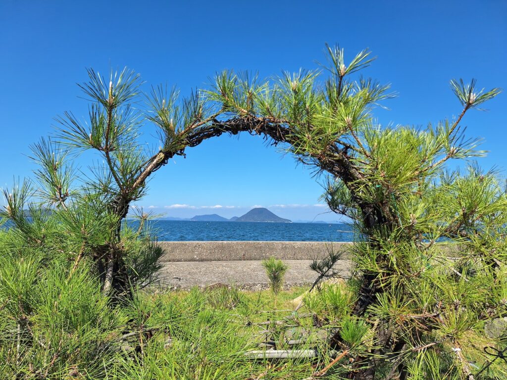 丸いトンネル状に整えられた松の枝の先に、青い海と空、美しい島々が見えます。