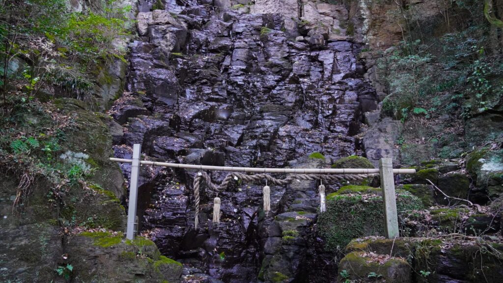 不動の滝が流れる城山のゴツゴツとした岩肌にしめ縄がかけられています