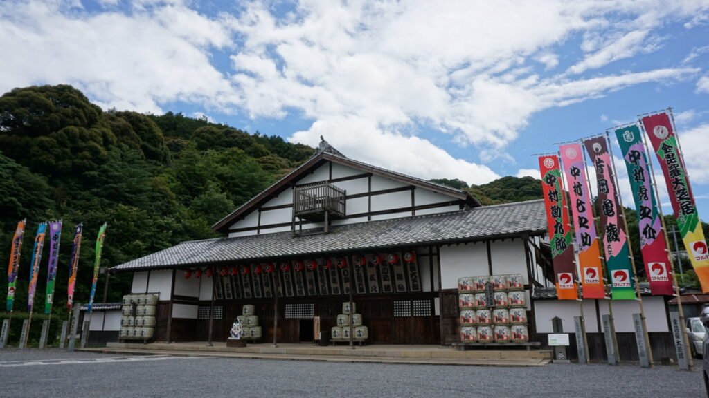 芝居小屋の左右には、５本ずつ旗が上げられている。正面には樽酒や歌舞伎公演者の名前が書かれた札や提灯が掲げられている。