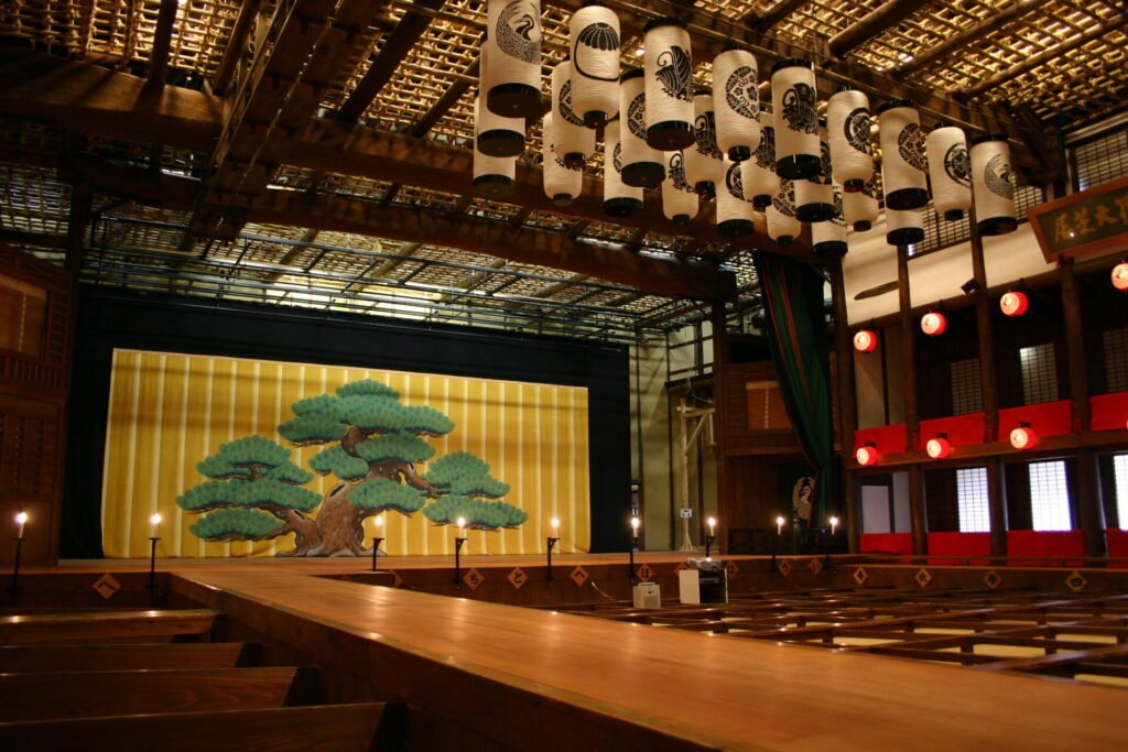 歌舞伎座のステージ。奥には松の幕がかかり、天井からは提灯が下げられている。中央には舞台への道があります。