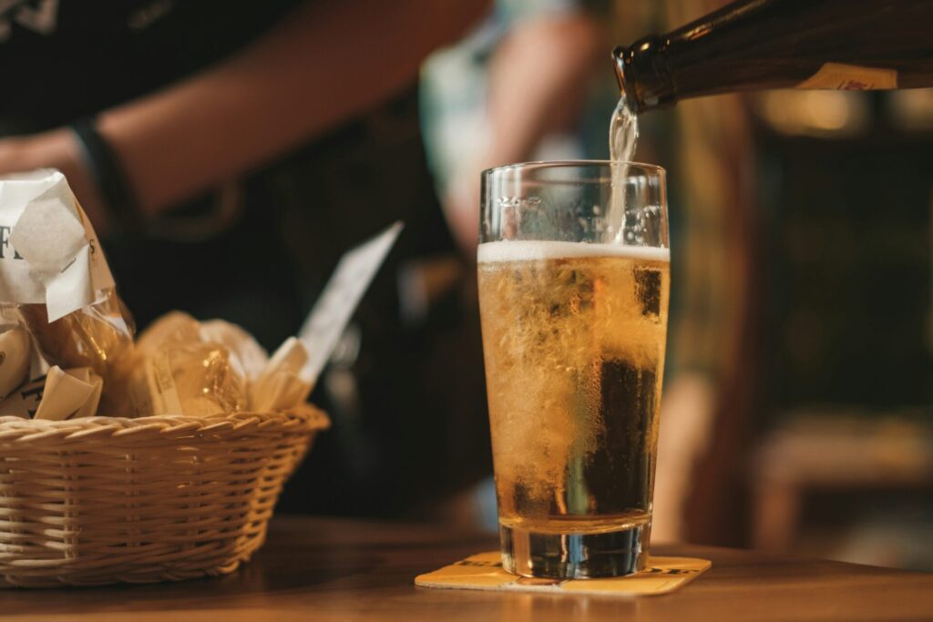 木のテーブルに置いてあるビアグラスに注がれるビールとカゴに入っているおつまみ。