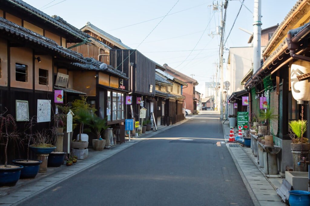 道路の左右に、昔ながらの木造の住宅が並んでいます。提灯や木の立て看板などがある風情ある光景です。