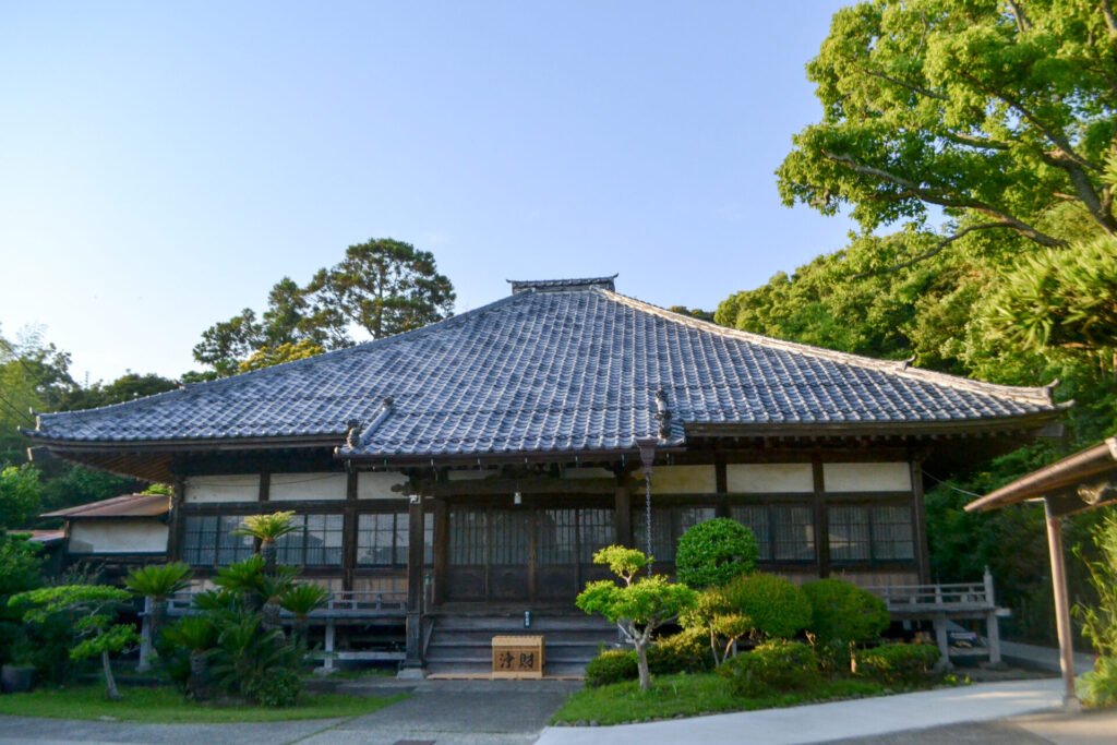 歴史を感じる木造建築物の浄楽寺。屋根は瓦葺きで、木製の引き戸が見えます。建物の前には手入れの行き届いた庭園があり、周囲は木々が建物を囲んでいます。