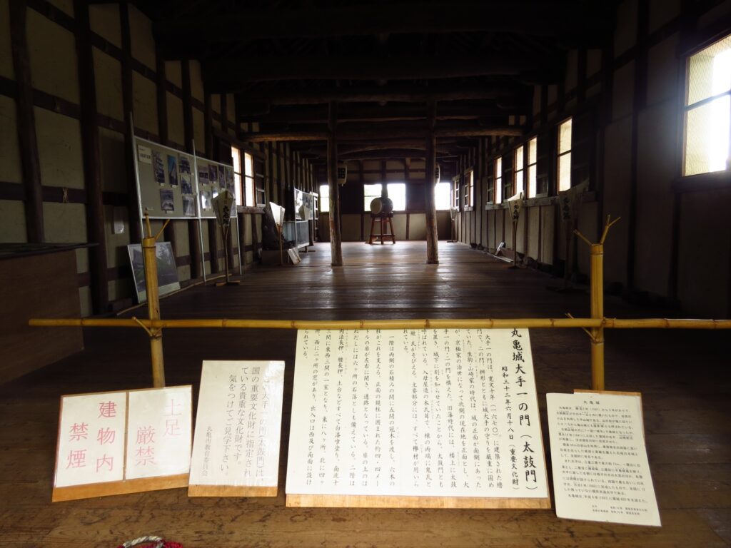 大手一の門（太鼓門）の櫓の内部。木造の柱と梁が見え、壁には写真や展示物が飾られています。手前には大手一の門の歴史と役割を説明する看板があり、窓からは柔らかな光が差し込んでいて、落ち着いた雰囲気が感じられます。