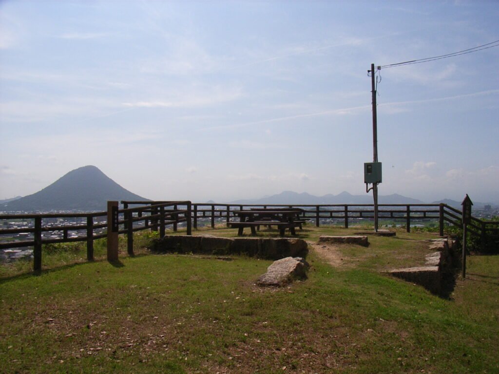 広々とした景色を望む月見櫓跡。手前には木製のフェンスとベンチが設置された草地が広がり、遠くには讃岐富士が見えます。