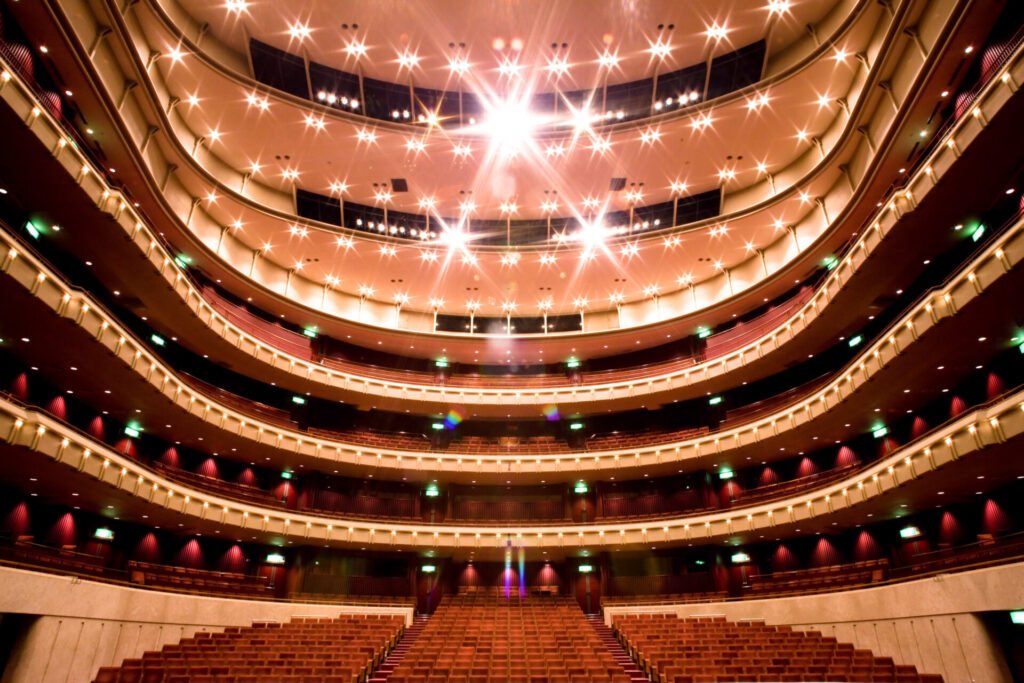 横須賀芸術劇場の大ホール。豪華な弧を描くように配置された客席と舞台。客席は複数階にわたって配置されており、各階層には赤い座席が整然と並んでいます。天井は、星のように見える明るい照明で飾られており、華やかな雰囲気を醸し出しています。