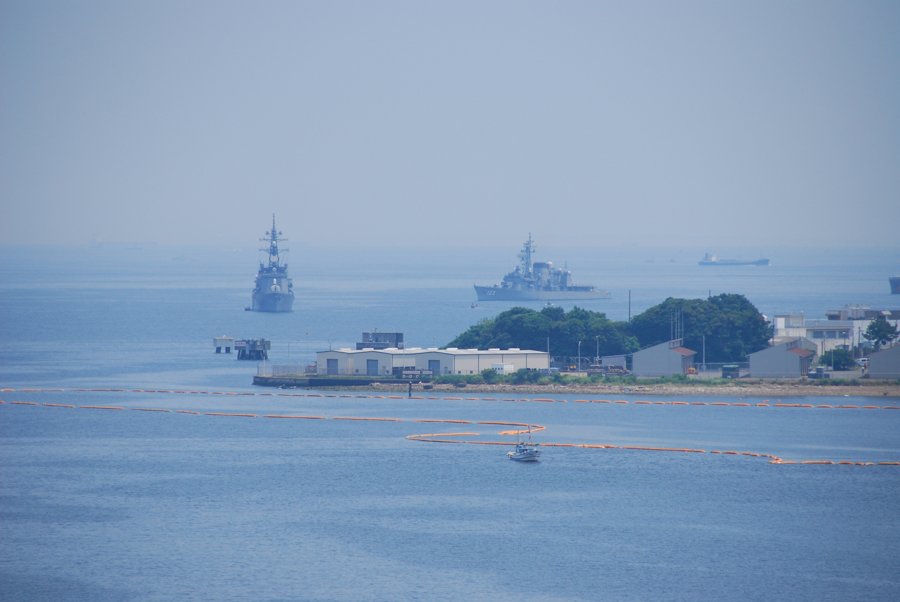 横須賀沖を航行する艦艇の遠景。穏やかな海と沿岸施設が見える