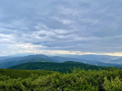 伊豆国方面の風景。緑豊かな山々が重なり合い、遠くには青くかすむ山々が見えます。空は厚い雲に覆われていますが、所々に明るい光が差し込み、山々の陰影が美しく際立っています。