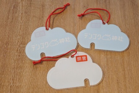 雲の形をした「テンゴク神社」の絵馬が三つ写っています。絵馬は薄い青色と薄い朱色の二種類で、「テンゴク神社」のロゴと「開雲」という文字が印刷されています。赤い紐が付いており、吊るすことができます。絵馬は願い事を書き込むスペースがあります。